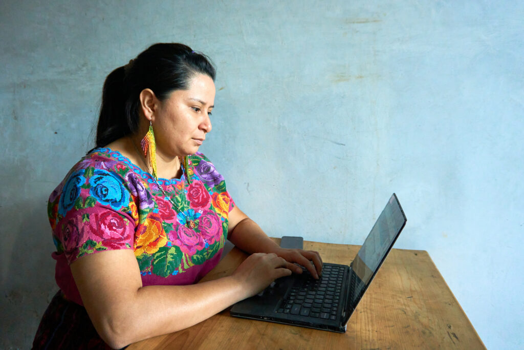 Photo of Guatemalan woman in traditional huipil dress working with laptop